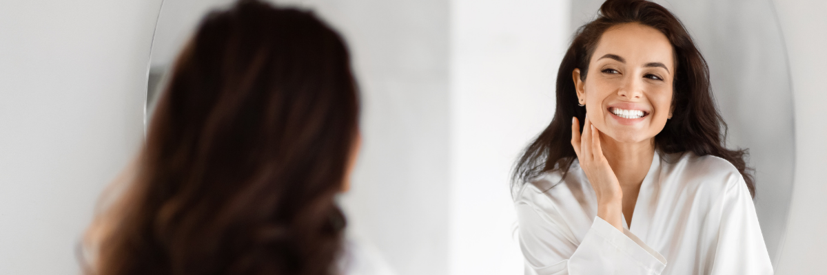 A lady looking in a mirror while using clear aligners from smiles club.